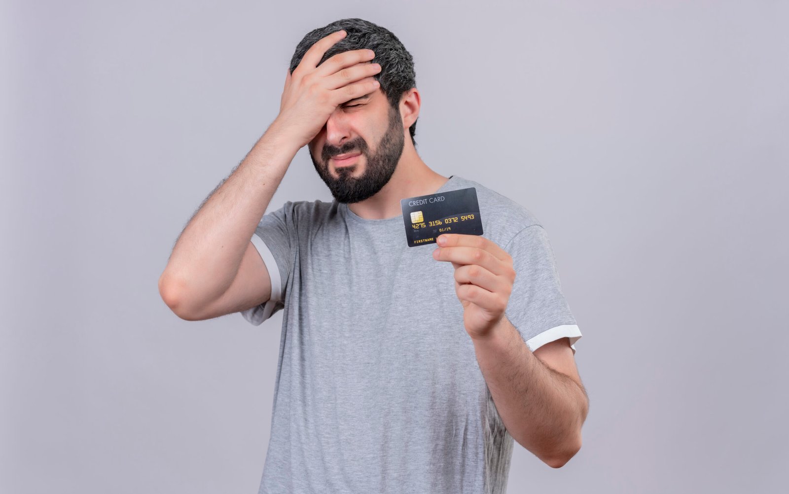 stressed young handsome caucasian man holding credit card and putting hand on head with closed eyes isolated on white background with copy space